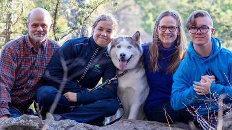 The Shergens, a family of four posing with their husky with sunny trees in the background