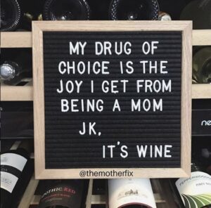 Decorative sign propped up on wine rack saying "My drug of choice is the joy I get from being a mom. Jk. It's wine."
