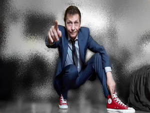 RJ Formanek crouched down in a suit and red converse shoes pointing at the camera with his right hand while his left hand rests on his bent knee.