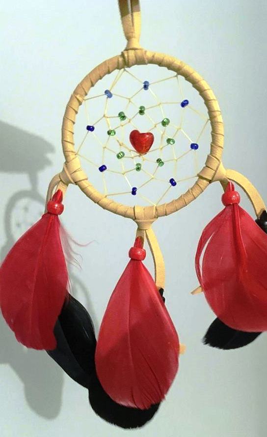 A dream catcher with three red and three black feathers dangling, green and blue beads, and a small red heart-shaped bead at the centre. 