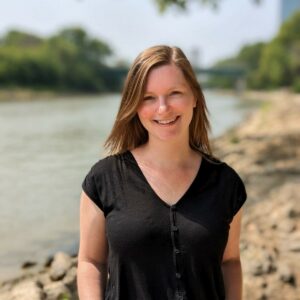 Melanie Muehling smiling at the camera in front of an out of focus background of a river bank