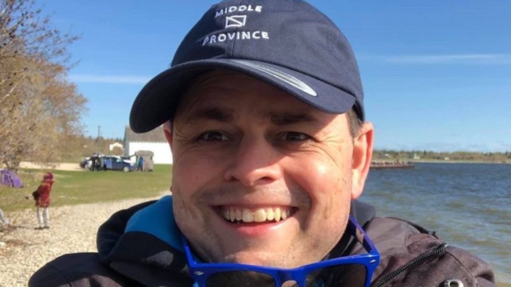 Man smiles in selfie in front of lake