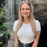Chantel Ritter A woman with long straight blonde hair stands in front of a stone waterfall.